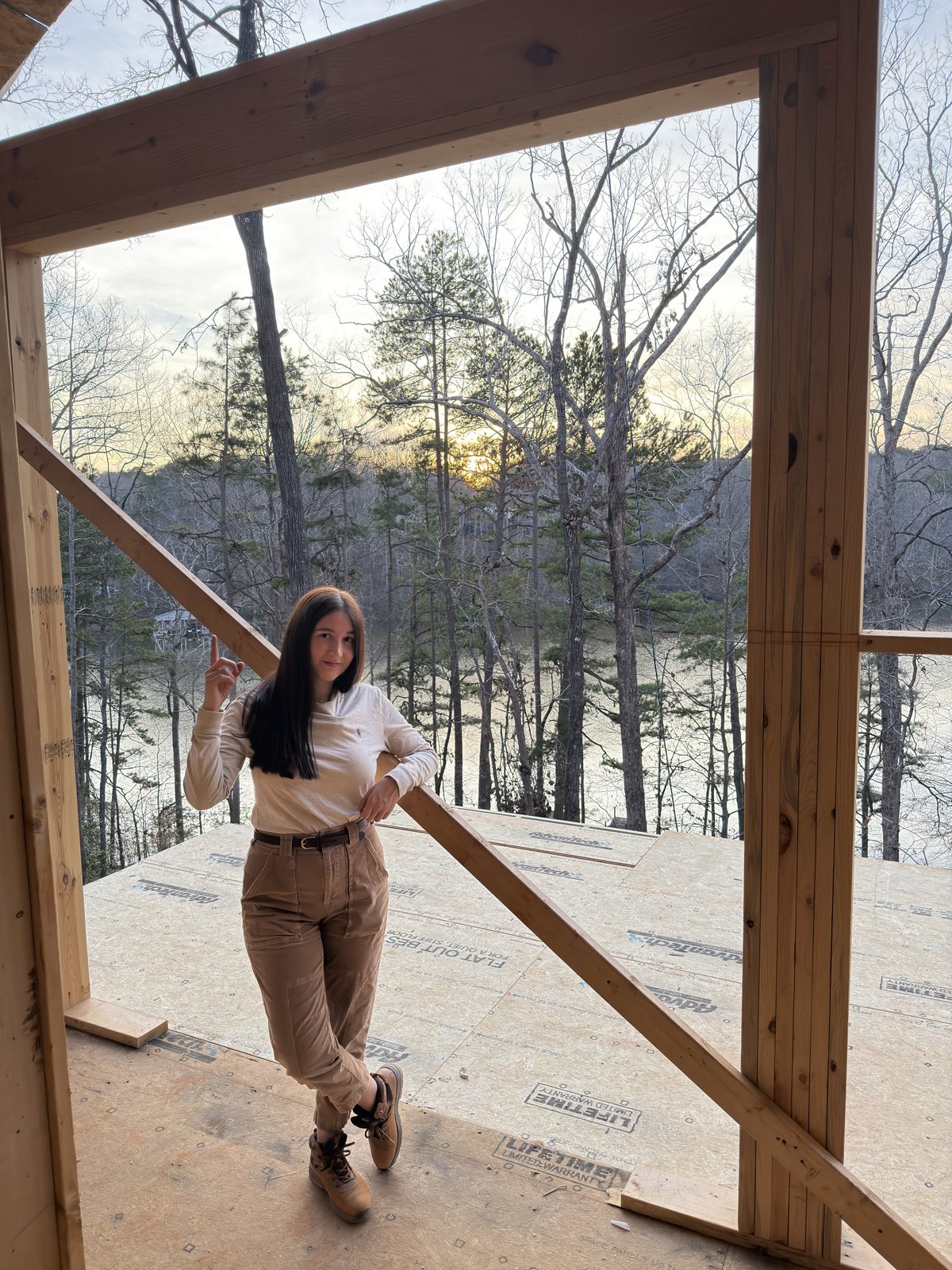 América Ahumada dentro de la estructura de madera de una casa en obra, al atardecer sobre el lago